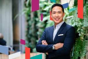 Business professional standing with arms crossed against a greenery backdrop.