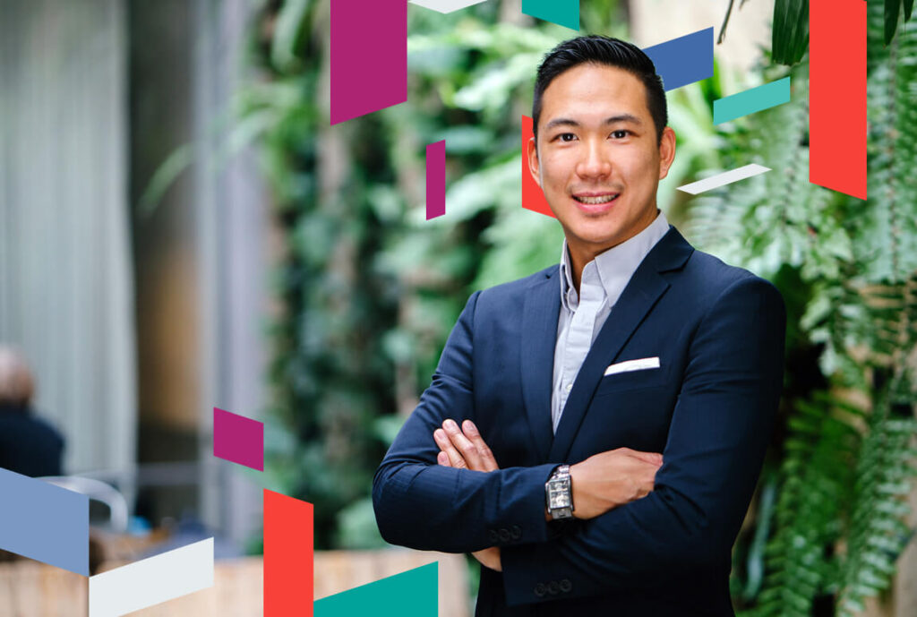 Business professional standing with arms crossed against a greenery backdrop.