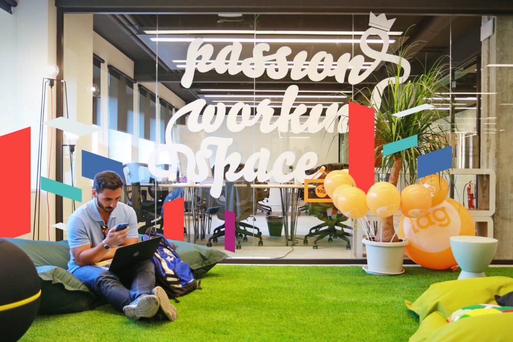 Young man working on laptop in modern office with 'passion working space' on glass wall.