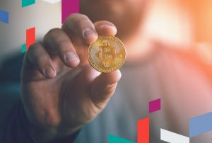 Person holding a Bitcoin coin with colorful design elements.