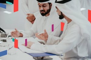 Two men in traditional attire discussing paperwork.