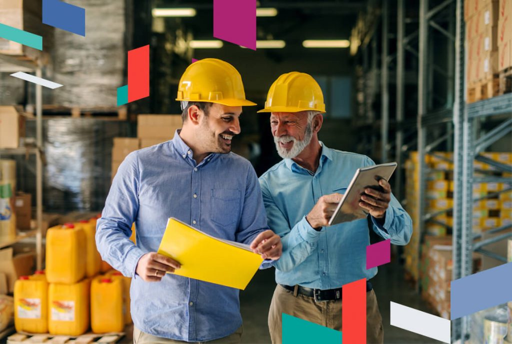 Two men in hard hats discussing in a warehouse with colorful shapes around them.