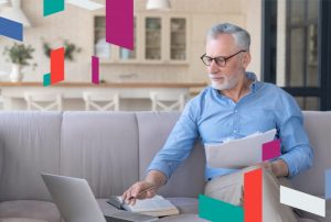 Man working on a laptop with paperwork, surrounded by colorful geometric shapes.
