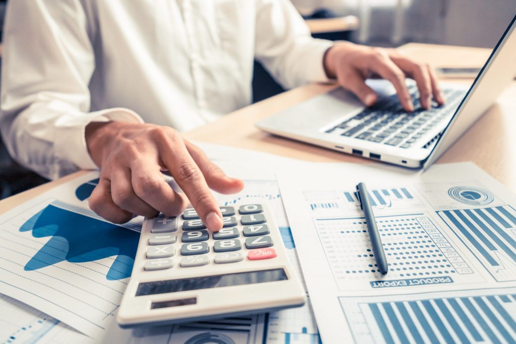 Person using a calculator and laptop with business documents on the desk.