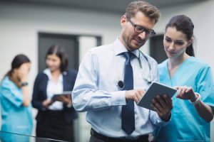 Professionals in medical attire discussing with tablet in hand.