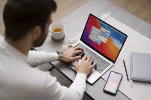 Person working on a laptop with a smartphone displaying an app and tea in the background.