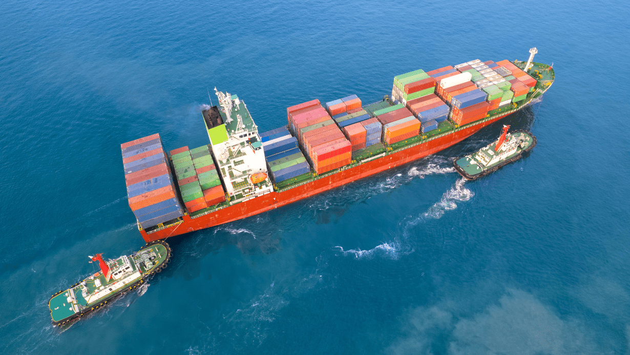 Cargo ship with containers escorted by tugboats at sea.