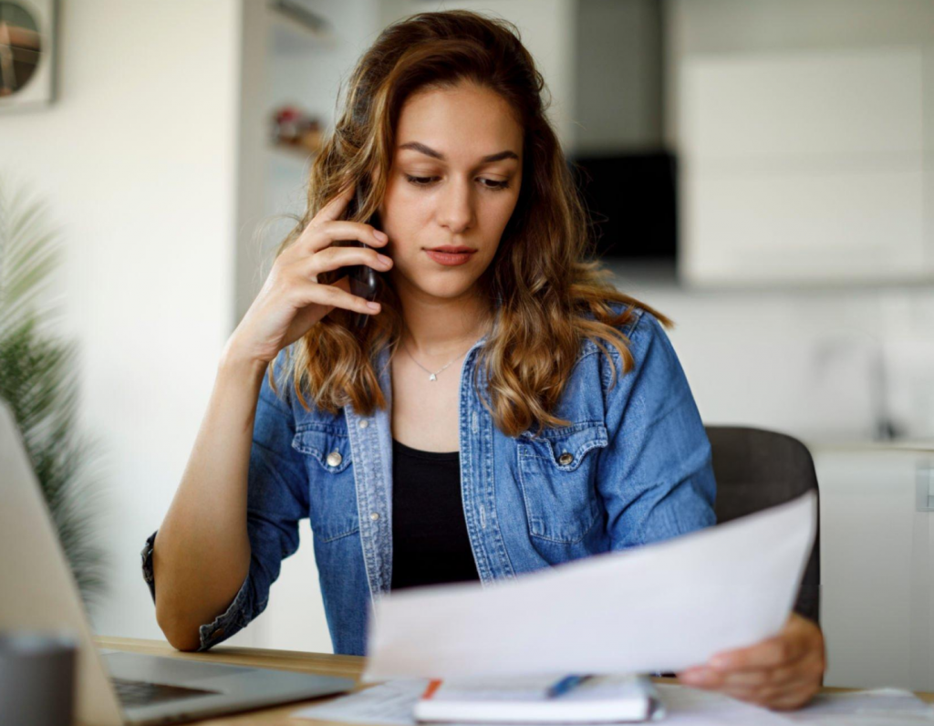 Woman on phone reviewing business documents at desk.