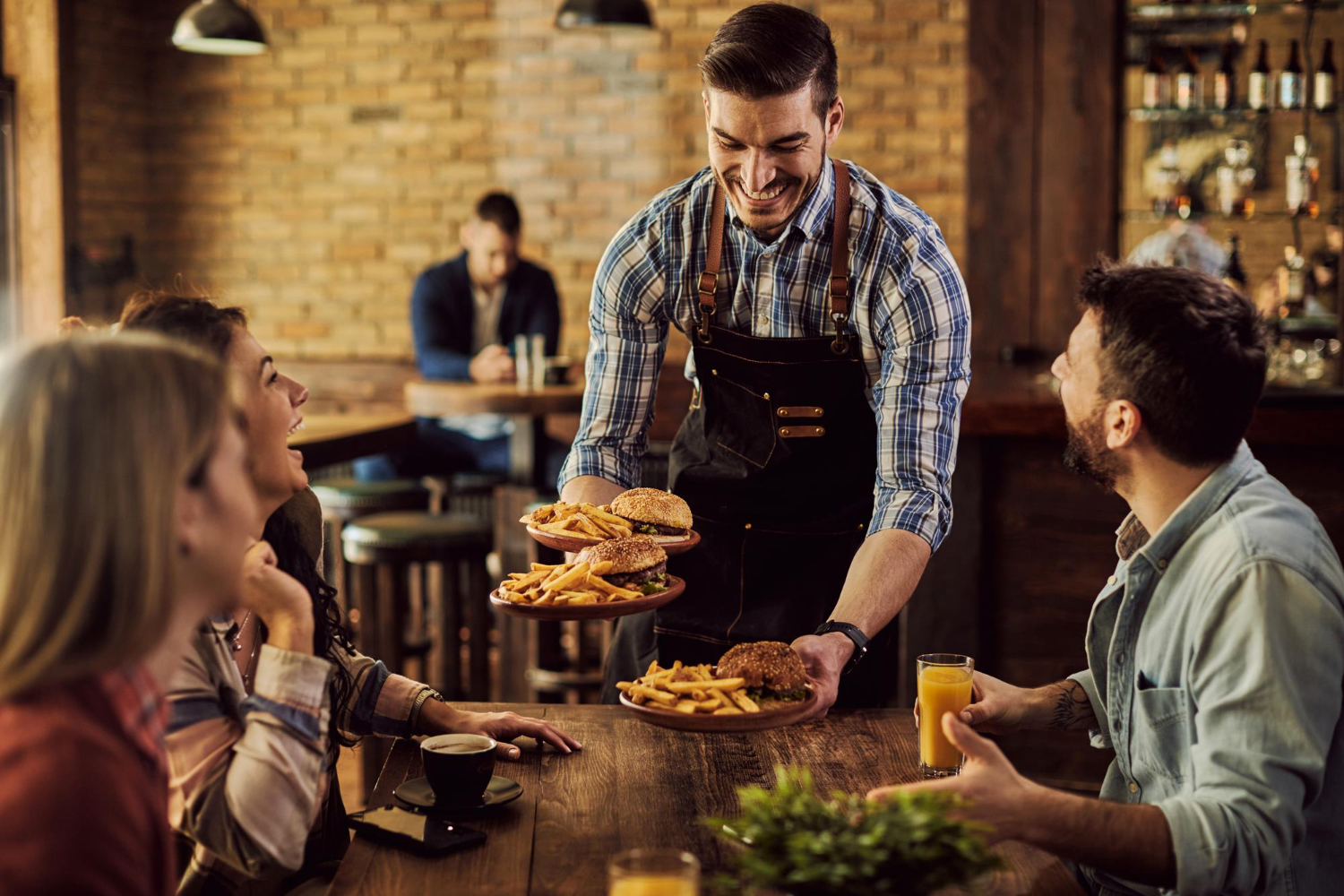 Group enjoying a meal served by a smiling waiter in a cozy restaurant.