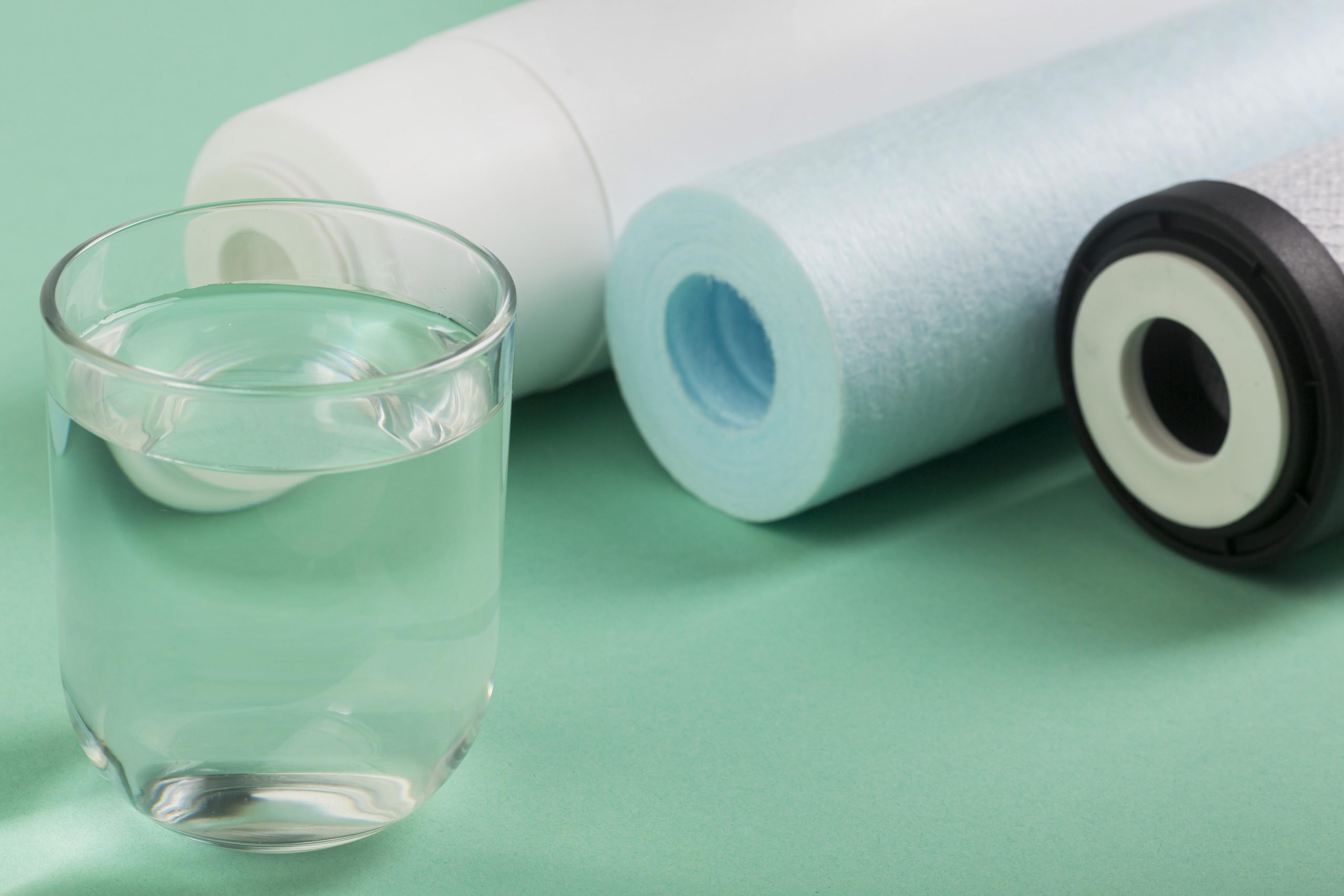 Glass of water beside filtration components on a green surface.