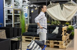 Woman pushing a cart in a store aisle with home goods.