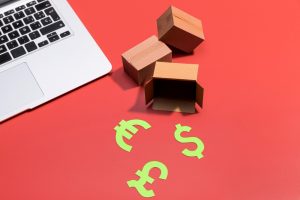 Laptop with cardboard boxes and currency symbols on red background.