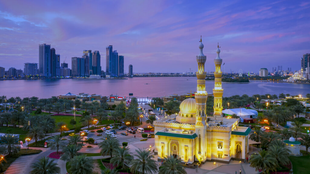 Sharjah skyline at sunset with waterfront, illuminated mosque, and city buildings in the background