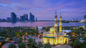Sharjah skyline at sunset with waterfront, illuminated mosque, and city buildings in the background